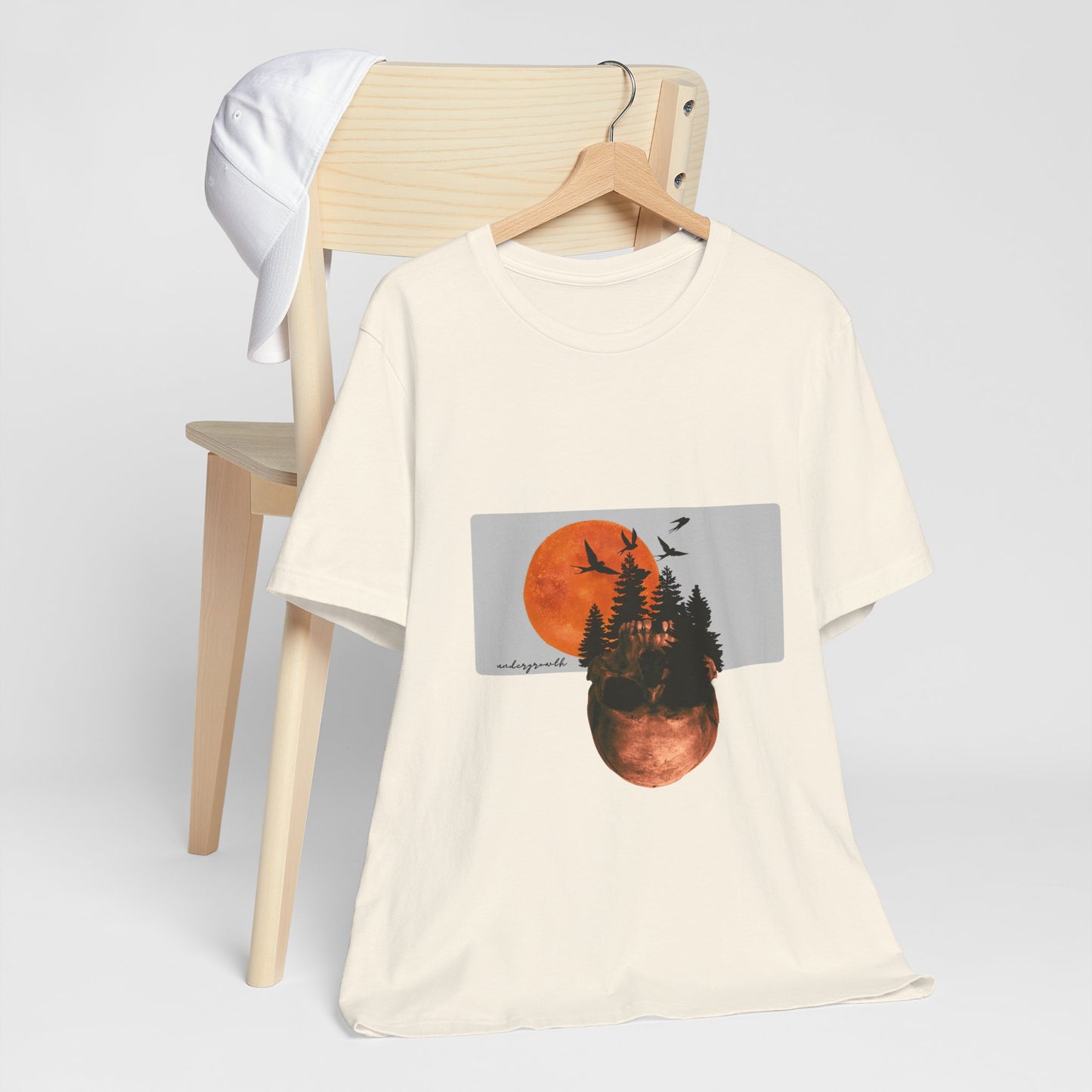 Beige t-shirt with nature-themed graphic on a wooden chair against a white background