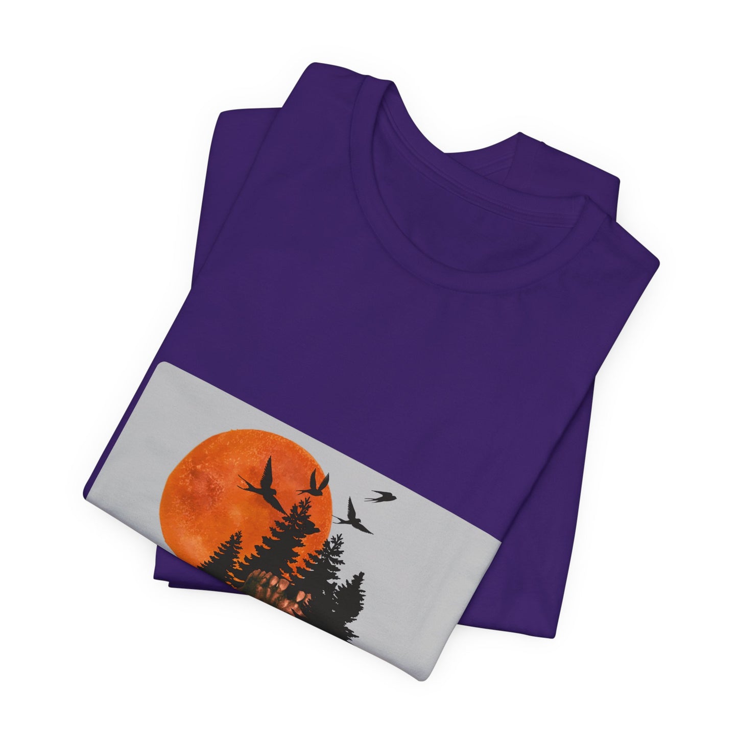 Folded purple t-shirt with a graphic of a sunset and trees on a white background