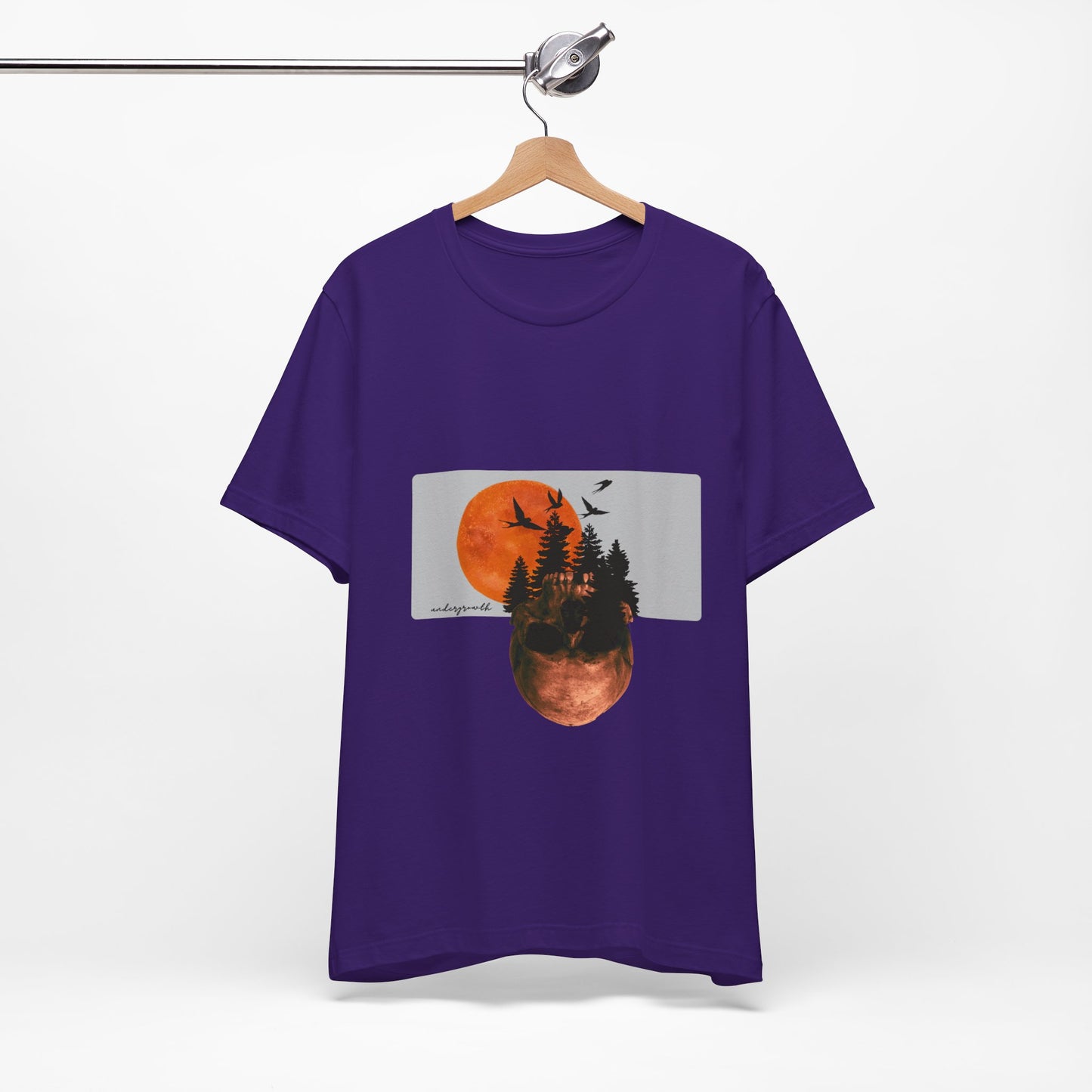 Purple t-shirt with a graphic design of trees and a sunset on a hanger against a white background