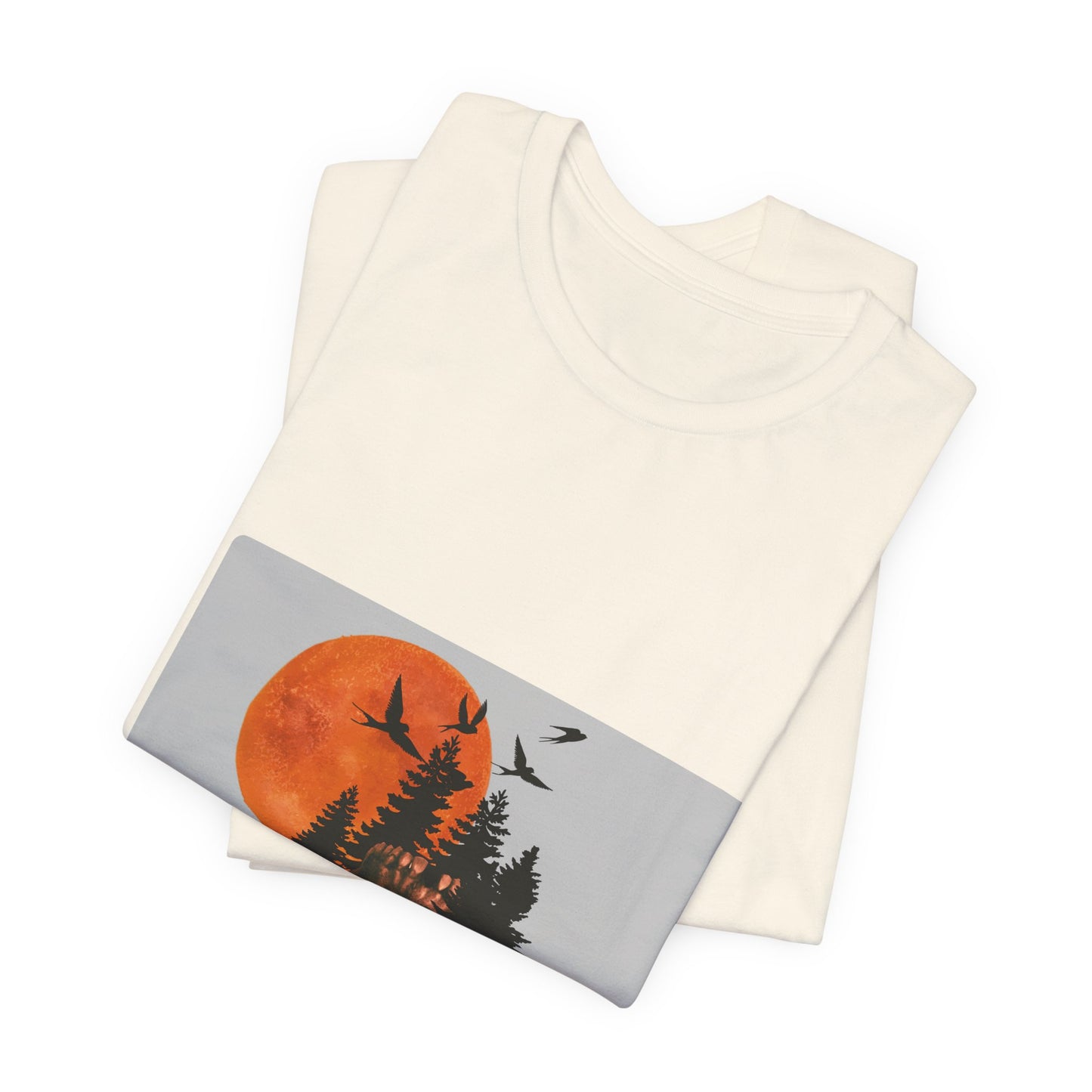 Folded natural color tee with graphic of skull and nature against neutral background.