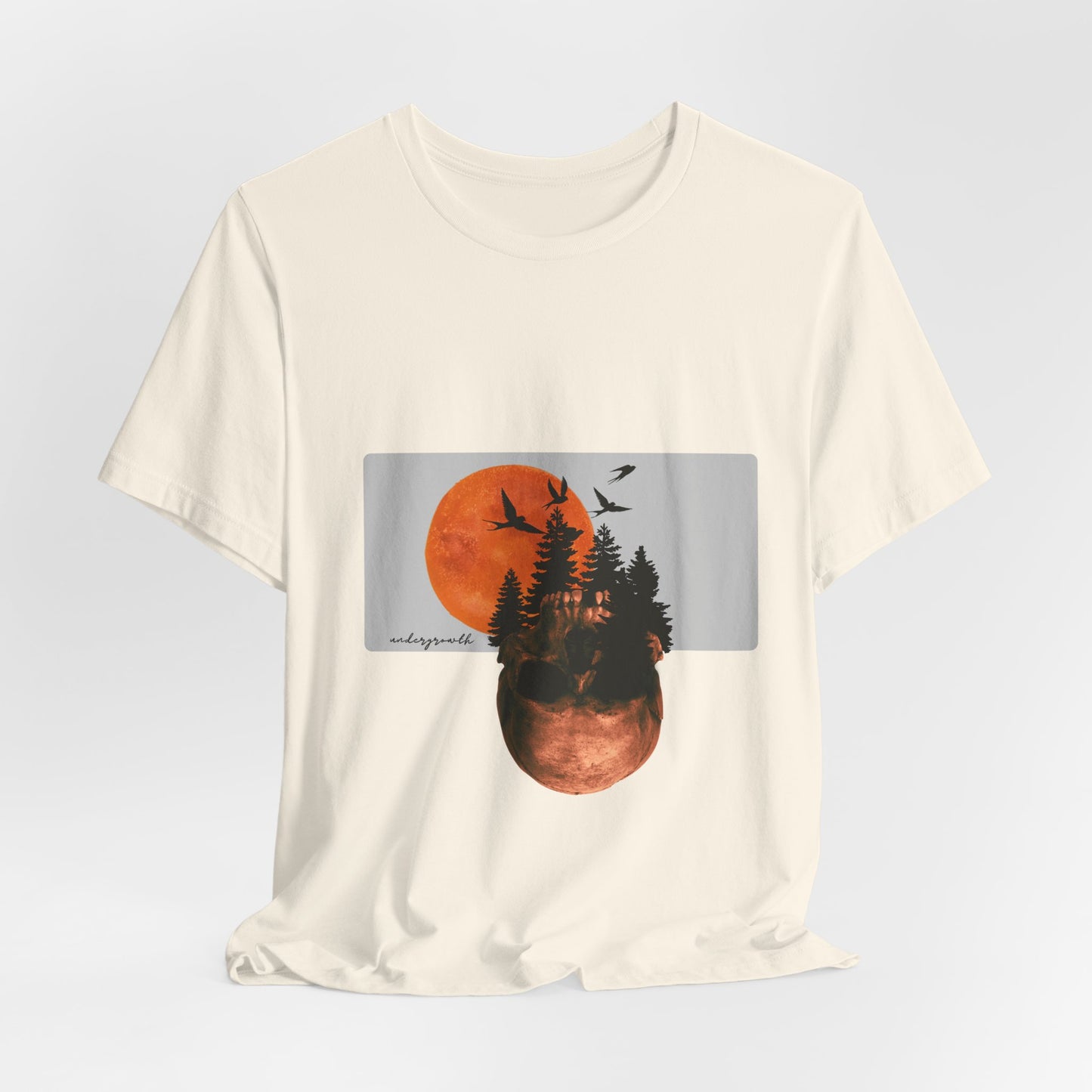 Beige t-shirt with a graphic of a sunset over trees and birds on a light gray background