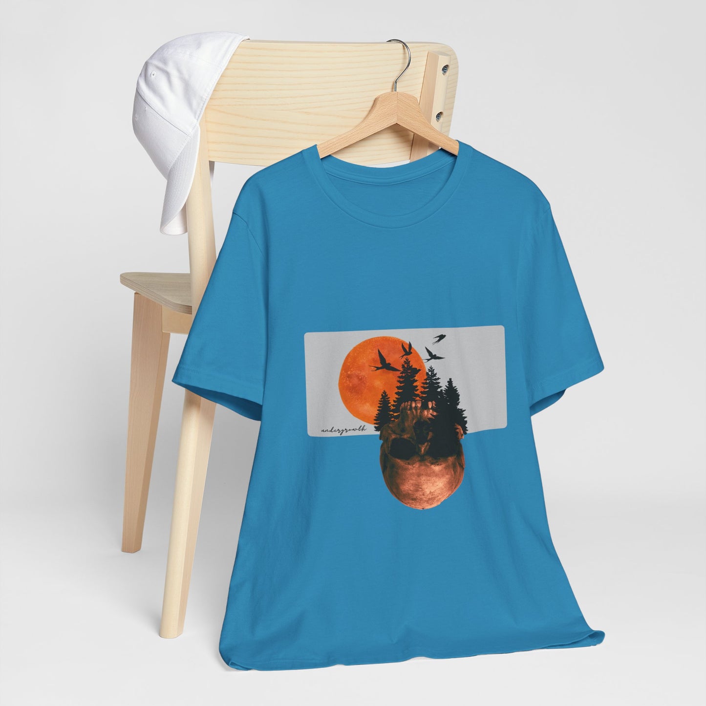 Blue t-shirt with a graphic design of a sunset over trees on a hanger against a white background.