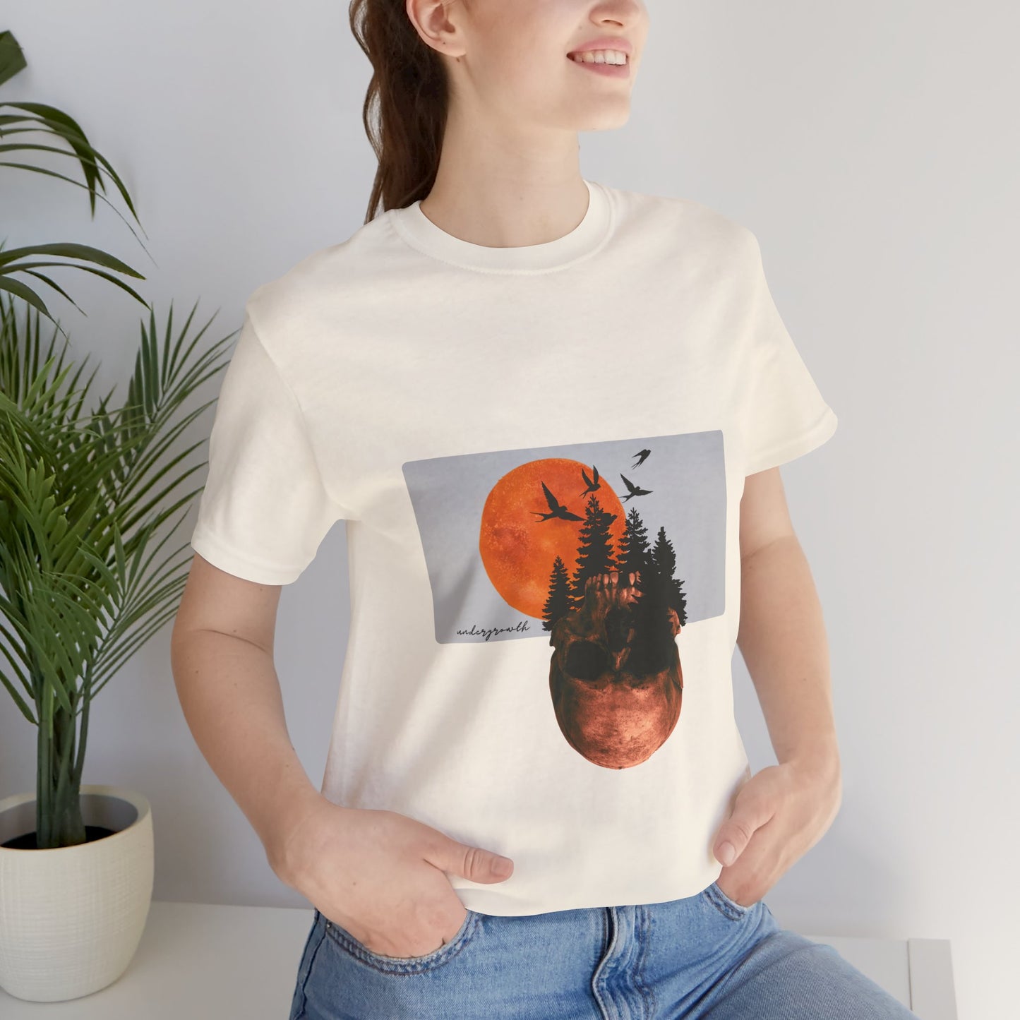 Person wearing a white t-shirt with a graphic design of trees and a moon.