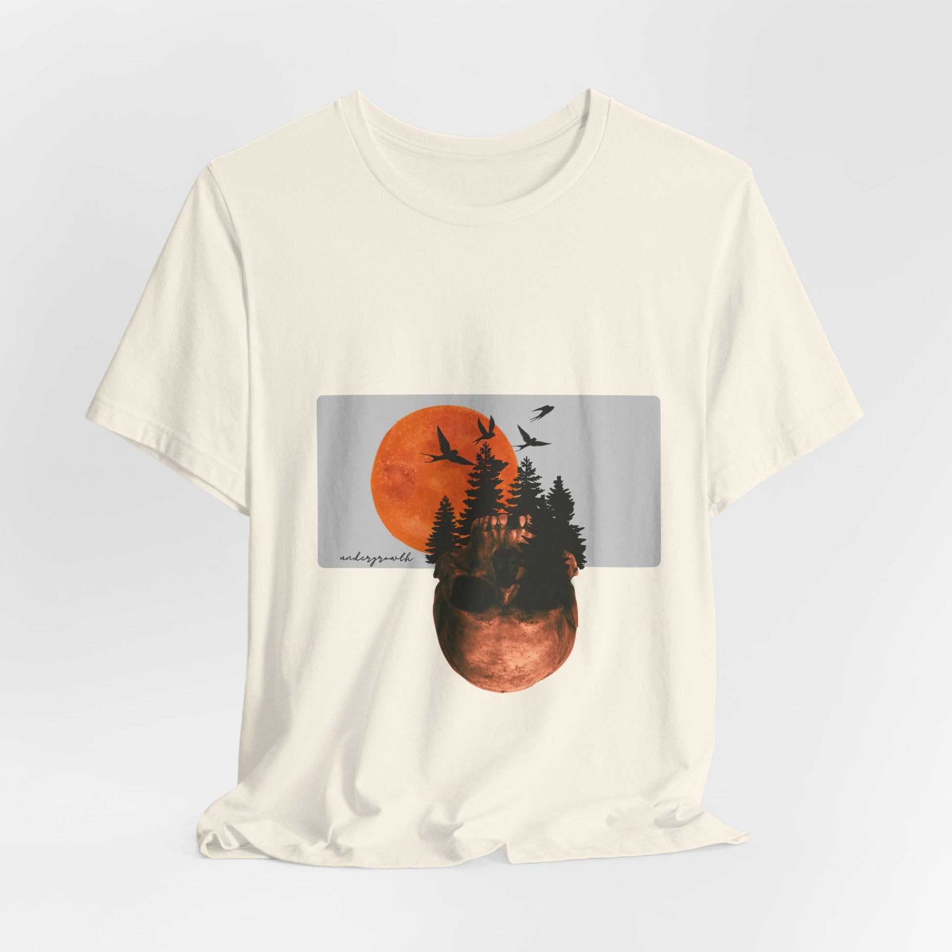 Beige t-shirt with a graphic of a sunset over trees and birds on a light gray background