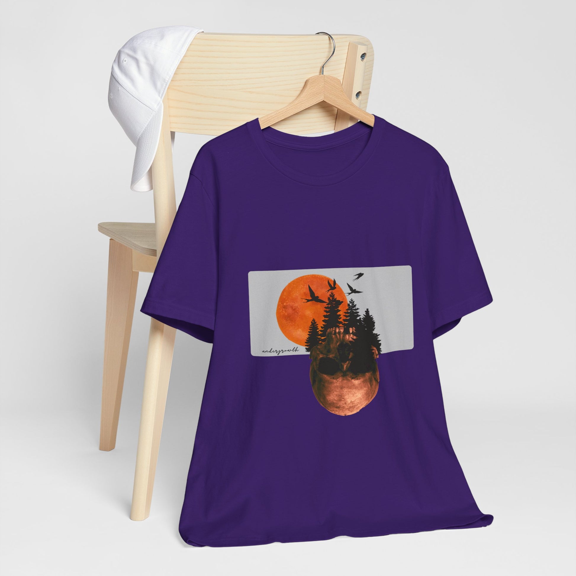 Purple t-shirt with nature graphic on a wooden chair against a white background